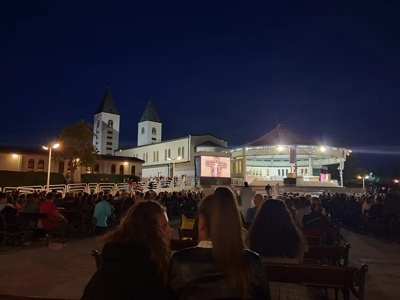 St James's church lit at night, with the outdoor altar to the right and the benches full of pilgrims