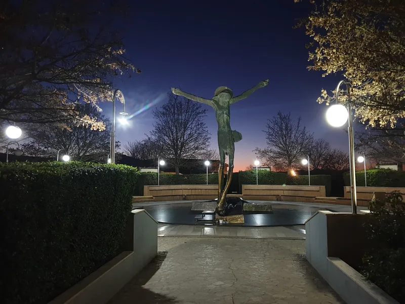 The Risen Christ statue at dusk, with lit lamp posts along the paved approach